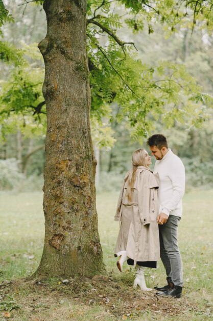 People in a park. Woman in a brown coat. Man in a white sweater.