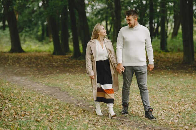 People in a park. Woman in a brown coat. Man in a white sweater.