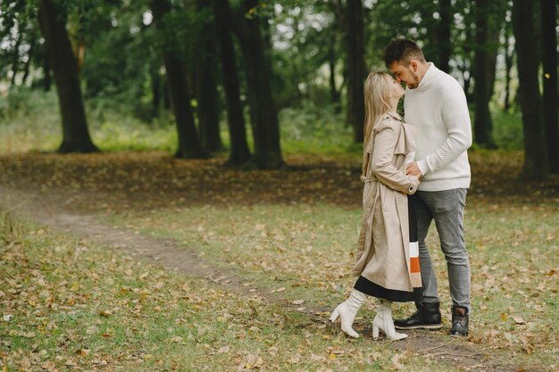 People in a park. Woman in a brown coat. Man in a white sweater.