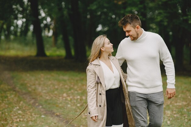 People in a park. Woman in a brown coat. Man in a white sweater.