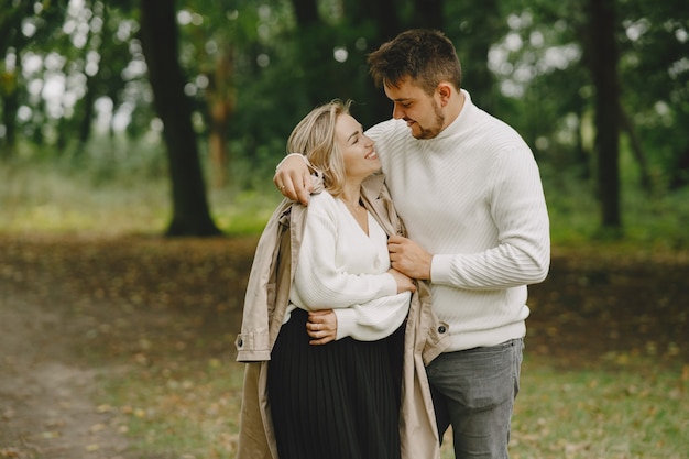 People in a park. Woman in a brown coat. Man in a white sweater.