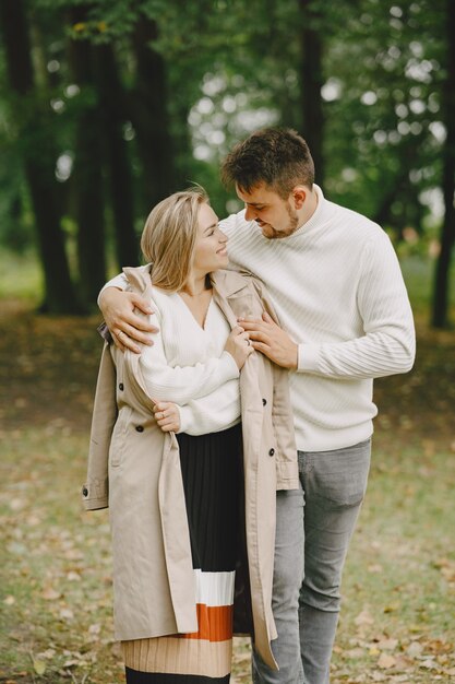 People in a park. Woman in a brown coat. Man in a white sweater.