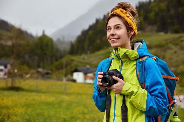 People, recreation, photographing. Satisfied traveler holds camera, rucksack, smiles positively