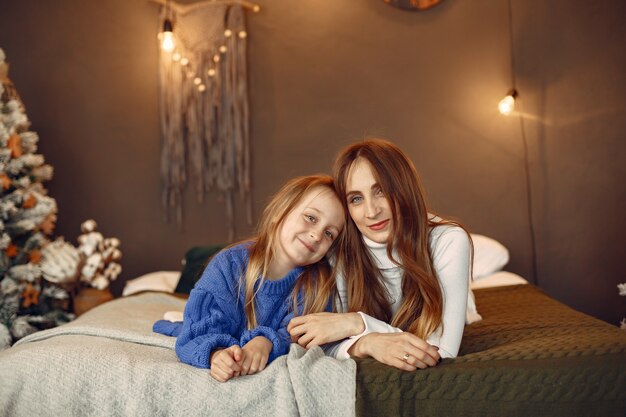 People reparing for Christmas. Mother playing with her daughter. Family is resting in a festive room. Child in a blue sweater.