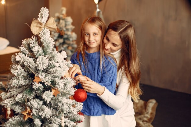 クリスマスの準備をしている人。娘と遊ぶ母。家族はお祭りの部屋で休んでいます。青いセーターを着た子供。