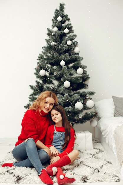 People reparing for Christmas. Mother playing with her daughter. Family is resting in a festive room. Child in a red sweater.