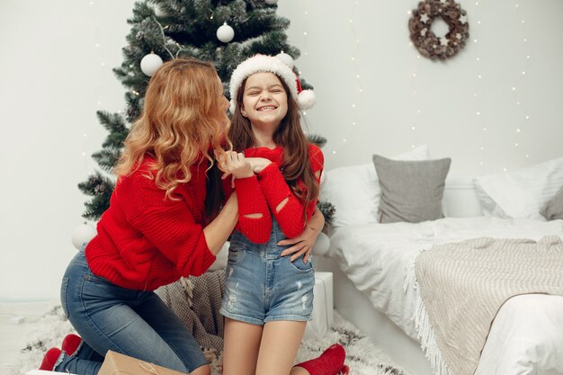 People reparing for Christmas. Mother playing with her daughter. Family is resting in a festive room. Child in a red sweater.