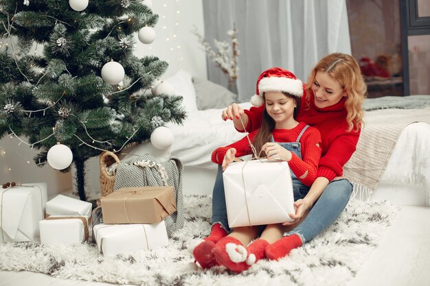 People reparing for Christmas. Mother playing with her daughter. Family is resting in a festive room. Child in a red sweater.