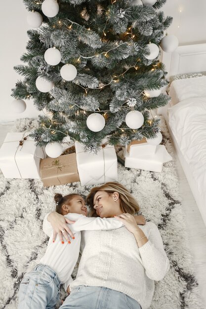 People reparing for Christmas. Mother playing with her daughter. Family is resting in a festive room. Child in a sweater sweater.