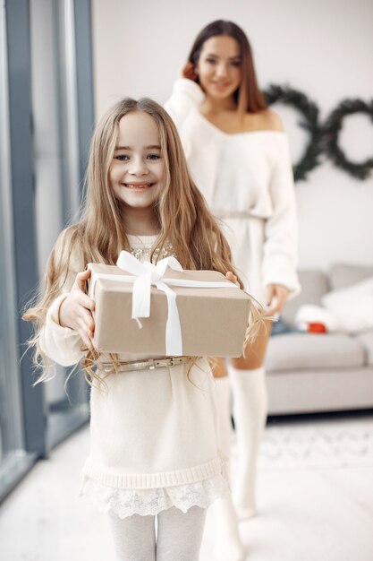 People reparing for Christmas. Mother playing with her daughter. Family is resting in a festive room. Little girl in a white dress.