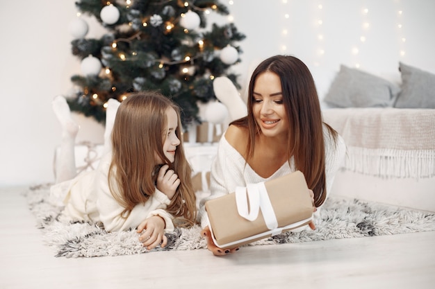 People reparing for Christmas. Mother playing with her daughter. Family sitting by the Christmass tree. Little girl in a white dress.