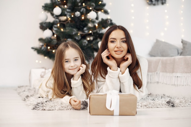 Persone che si preparano per il natale. madre che gioca con sua figlia. famiglia seduta vicino all'albero di natale. bambina in un vestito bianco.