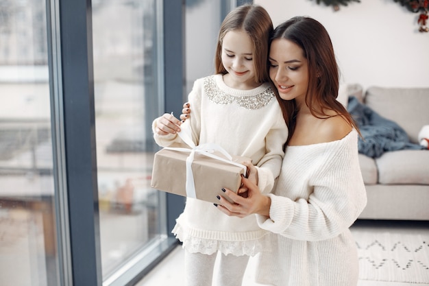 Persone che si preparano per il natale. madre che gioca con sua figlia. famiglia in piedi vicino alla finestra. bambina in un vestito bianco.