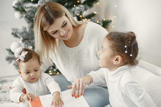 People reparing for Christmas. Mother playing with her daughters. Family is resting in a festive room. Child in a sweater sweater.