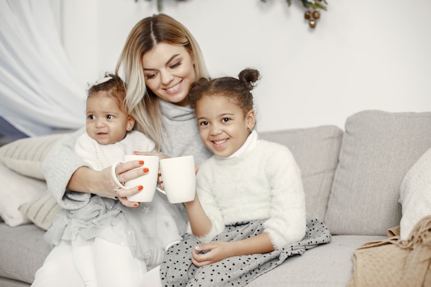 People reparing for Christmas. Mother playing with her daughters. Family is resting in a festive room. Child in a sweater sweater.