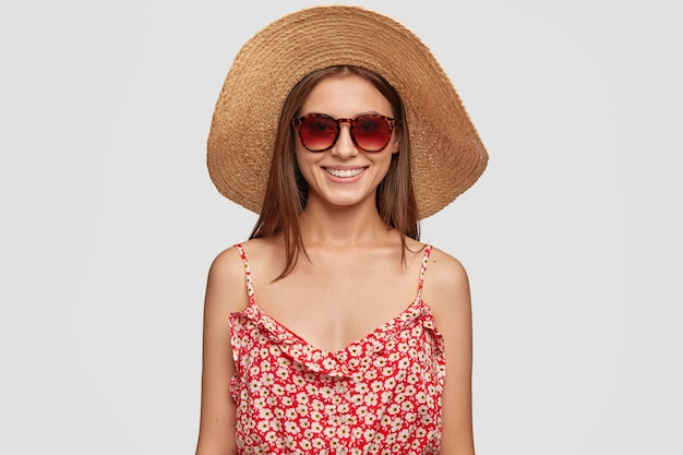 People and rest concept. Lovely satisfied female tourist in trendy shades, summer hat and dress. Tourist has vacation