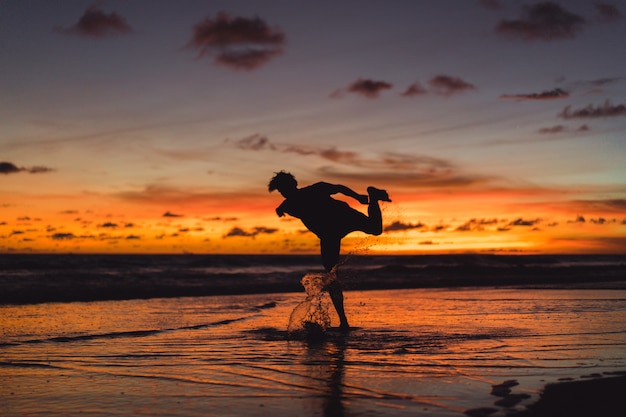 people on the shore of the ocean at sunset. man jumps against the backdrop of the setting sun