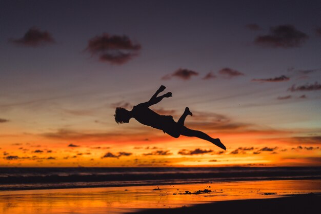 日没時に海岸の人々。人は夕日を背景にジャンプする