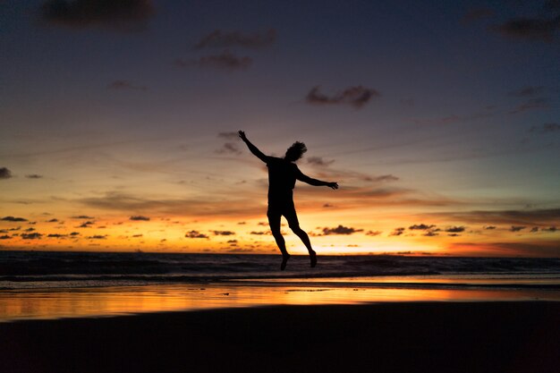 people on the shore of the ocean at sunset. man jumps 