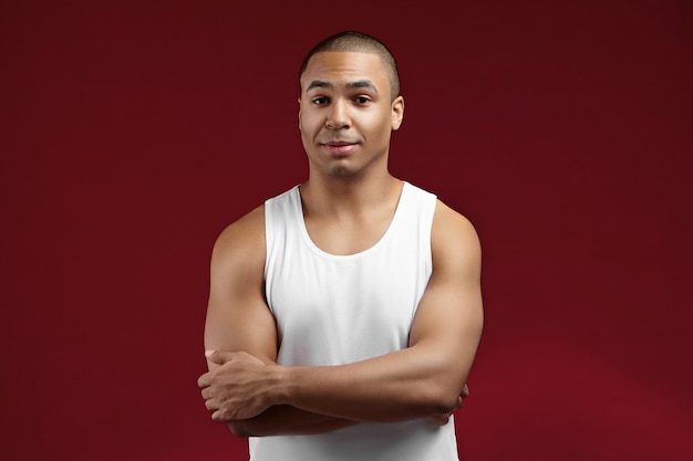 Free photo people, sports, fitness and active healthy lifestyle concept. attractive fit young mixed race male with muscular shoulders posing in studio, keeping arms folded, his look expressing confidence