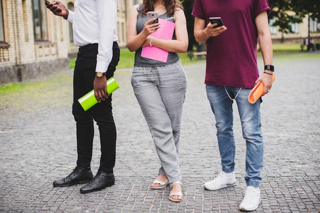 People standing holding notebooks looking on smartphones