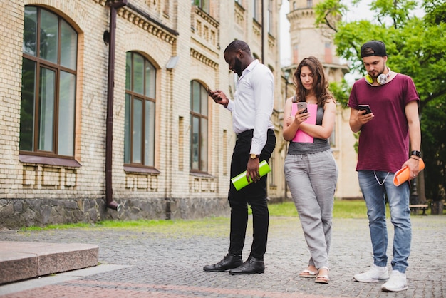 People standing holding notebooks looking on smartphones