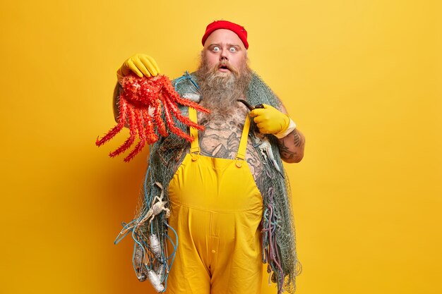 People sudden reaction concept. Bearded overweight male seafarer holds big red octopus stares with stupor