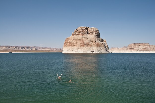 People swimming in the water near a big rock with a clear sky