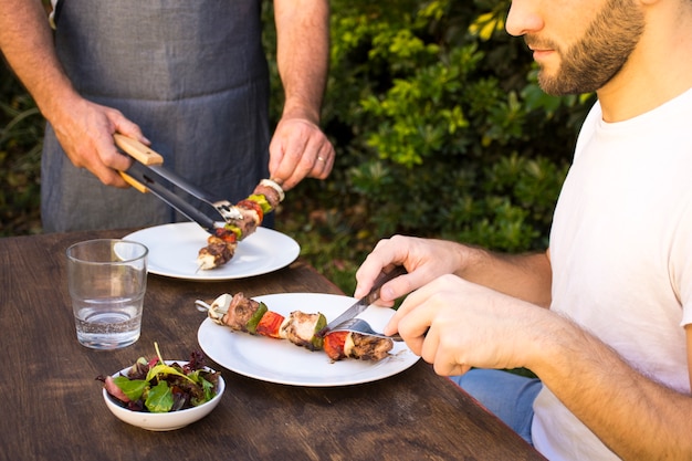 People tasting cooked barbecue in plates on table 