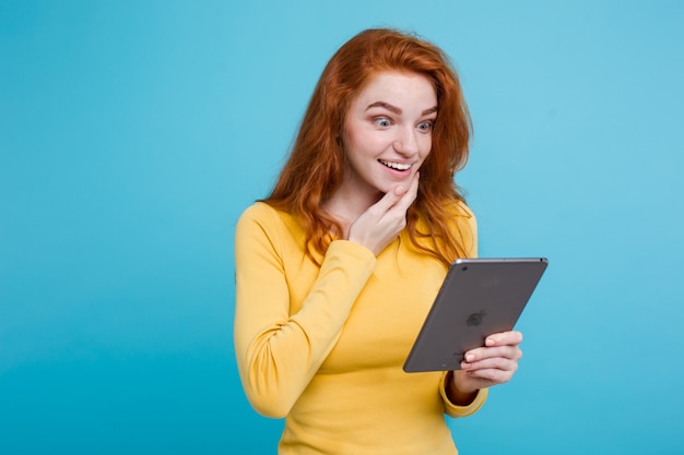 Люди и концепция технологии - закрыть Портрет молодой красивый привлекательный рыжий девушка счастлив улыбается на цифровой стол с чего-то что-то. Голубой пастельный фон. Копирование пространства.