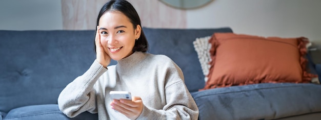 Free photo people and technology smiling asian woman sitting at home using her mobile phone typing message