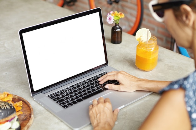 People and technology. Woman in shades browsing internet on her generic laptop, keyboarding