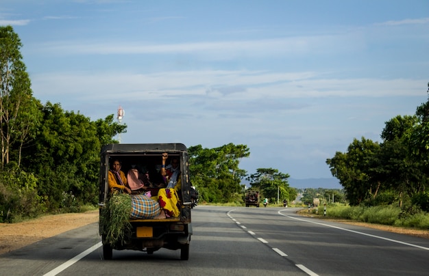 People traveling in the back of a crammed vehicle down a road in India