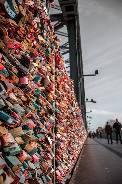 People walking on sidewalk with assorted-color padlocks on fence