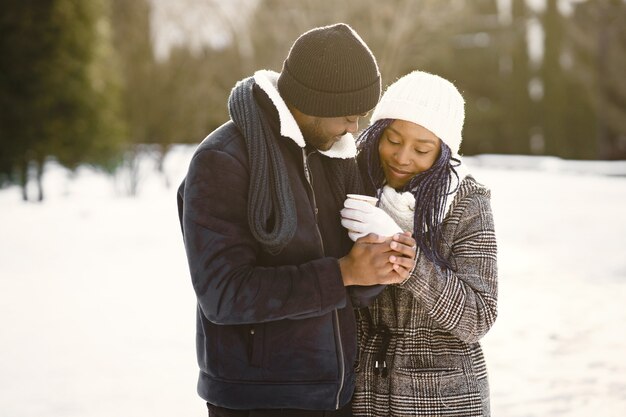 People walks outside. Winter day. African couple with coffee.