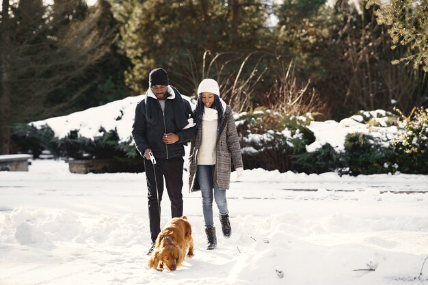 People walks outside. Winter day. African couple with dog.