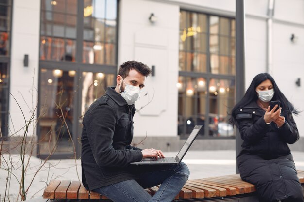 Люди в защитной маске сидят в городе с помощью электронных устройств