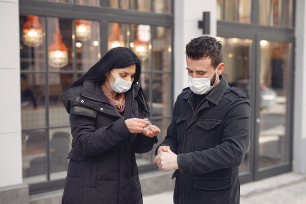Люди, носящие защитную маску, стоят на улице, используя спиртовой гель