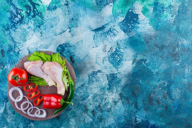 Pepper, onion rings, tomato, lettuce and chicken drumsticks on a board, on the blue background. 