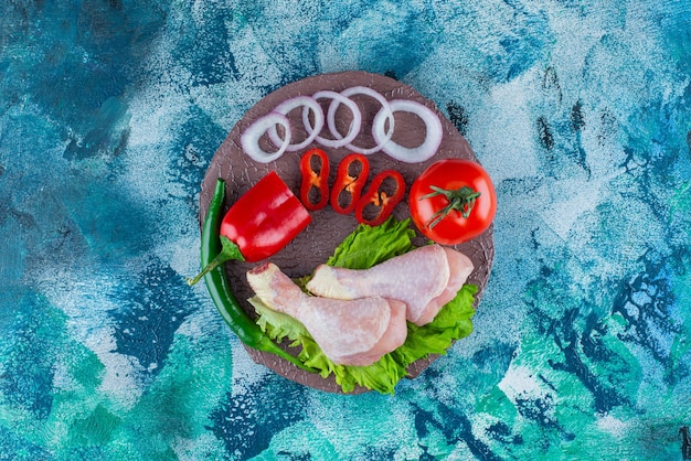 Pepper, onion rings, tomato, lettuce and chicken drumsticks on a board, on the blue background.