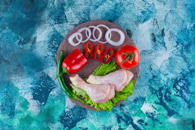 Pepper, onion rings, tomato, lettuce and chicken drumsticks on a board, on the blue background. 