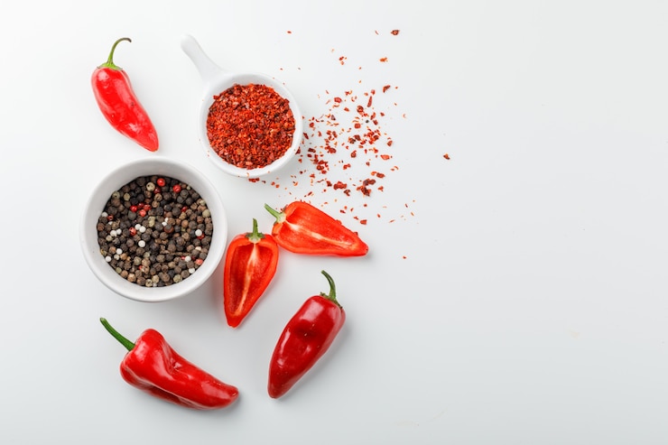 Free Photo peppercorns with chili powder in scoop and red peppers in a plate on white wall, top view.