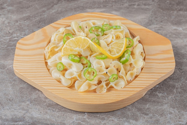 Peppered farfalle pasta with lemon slice on wooden plate , on the marble.