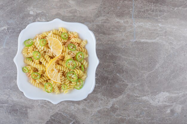 Peppered fusilli pasta with lemon slice on wooden plate , on the marble surface.