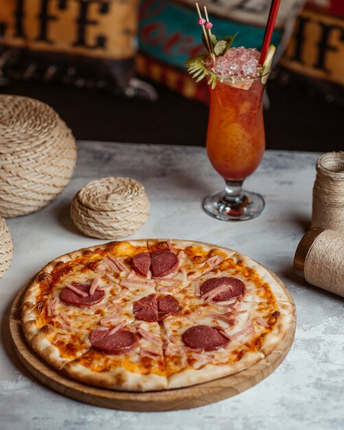 Pepperoni pizza on a wooden board with a glass of cocktail.