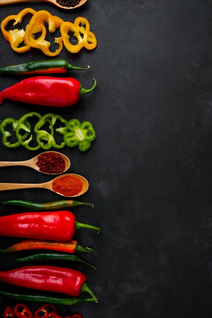 peppers and spoons of spices on black table