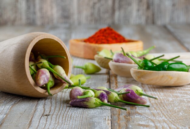 Peppers in spoons and vase with red pepper flakes side view on a wooden