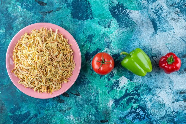 Peppers, tomatoes and noodle in a plate, on the blue table. 