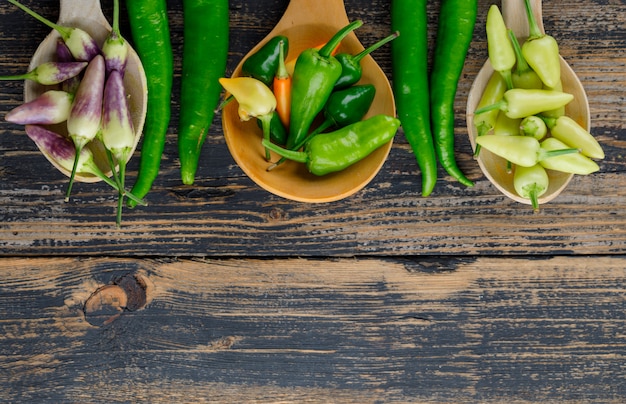 Free photo peppers in wooden spoons flat lay on a wooden