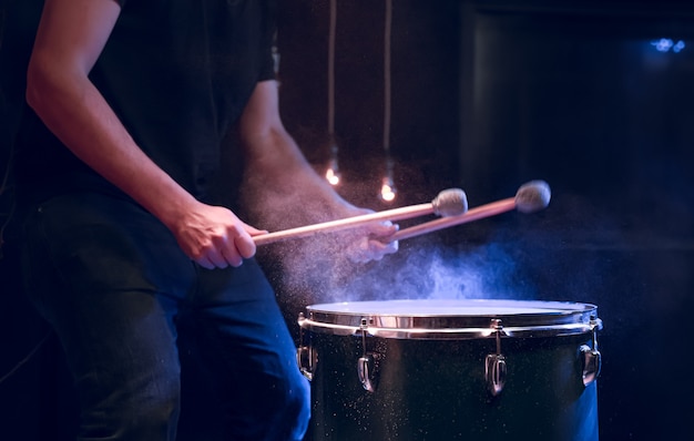 The percussionist plays with sticks on the floor tom on under studio lighting.. Concert and performance concept.